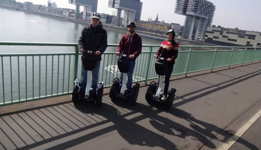 Drei Segway Fahrer in Köln auf einer Brücke vor den Kranhäusern
